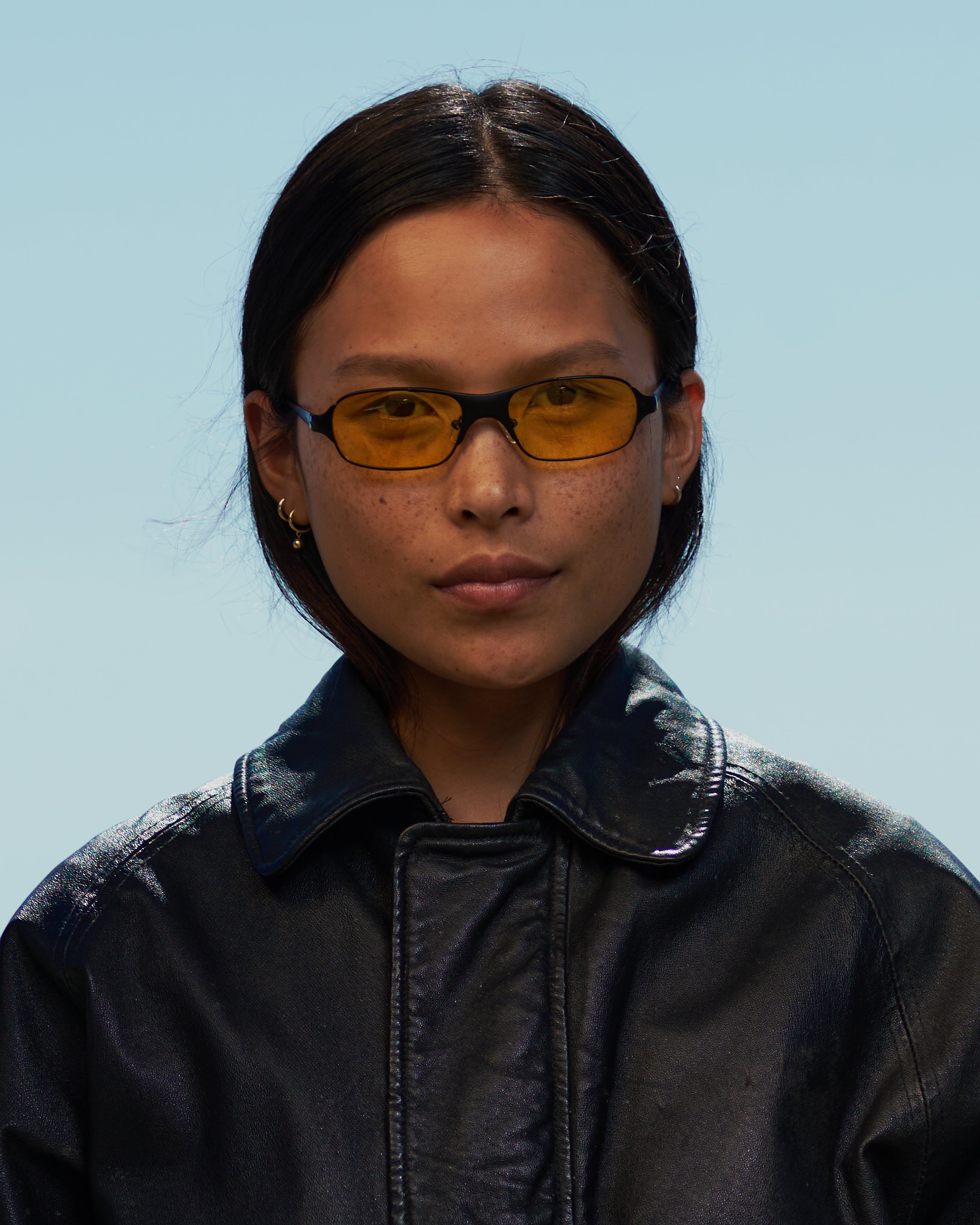 Women with dark hair in 90s / 2000s small frame glasses with yellow lenses and a black frame